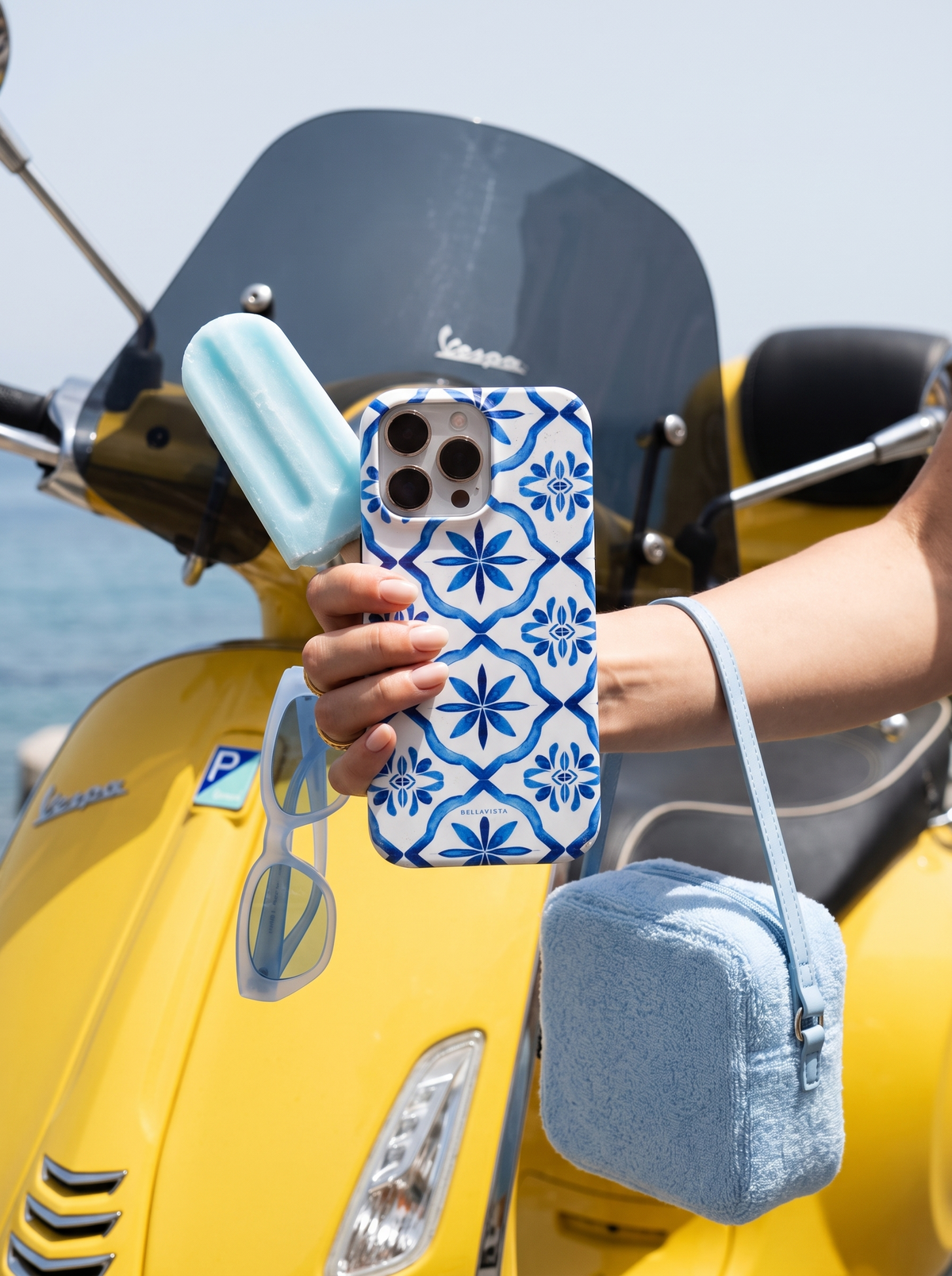 Maiolica Blu phone case held beside a yellow Vespa by the sea